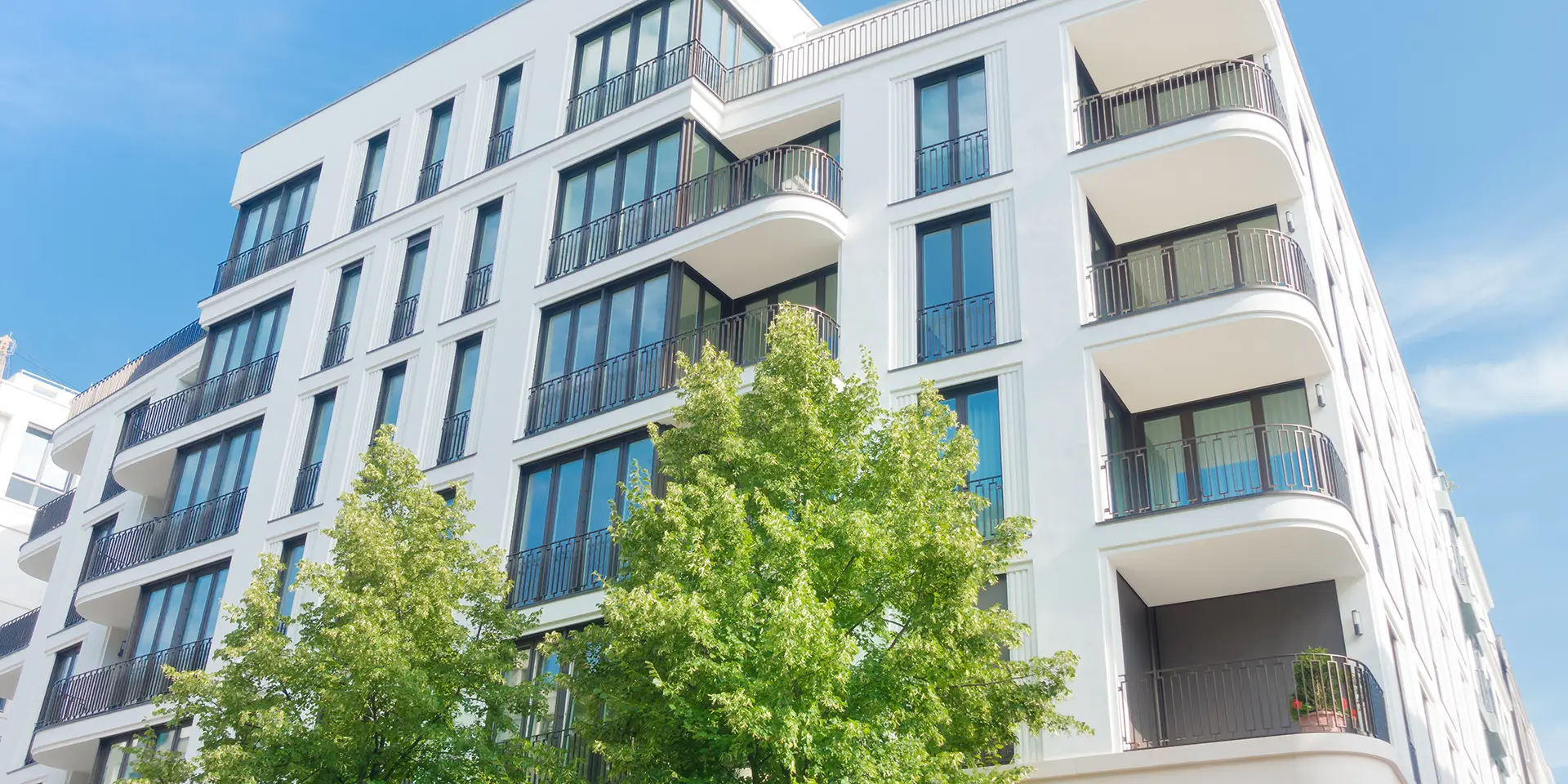 Modernes Mehrfamilienhaus mit mehreren Etagen, großen Glasfronten und Balkonen.